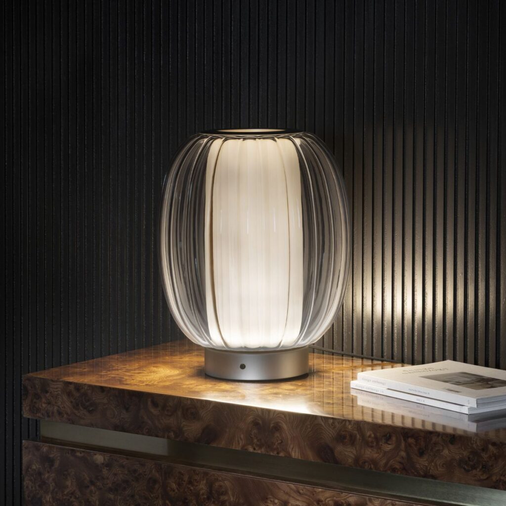 Lampada da tavolo Contardi Alma con il diffusore in vetro plissettato, su un mobile