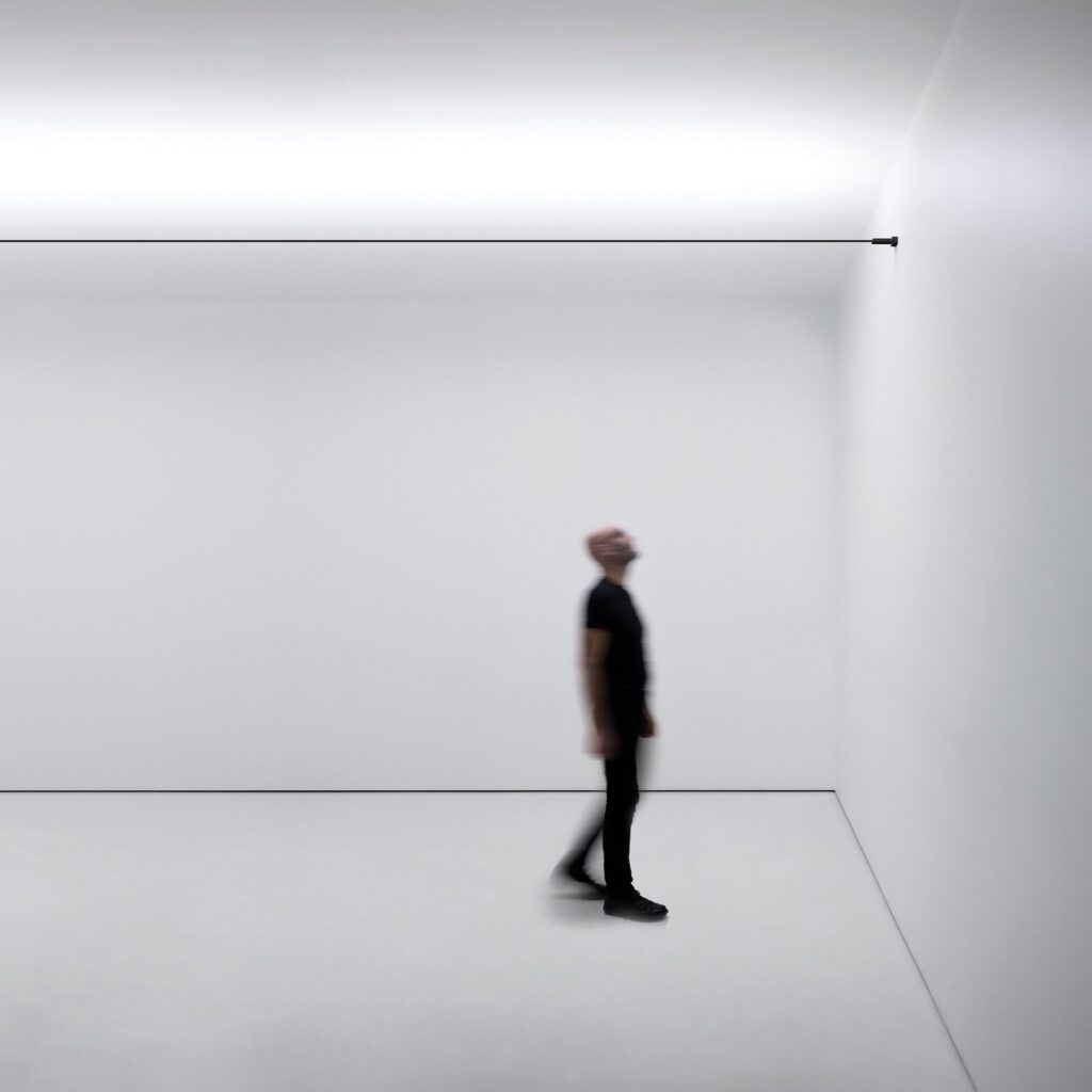 Stanza bianca con la linea di luce Davide Groppi Infinito a soffitto e una persona che cammina
