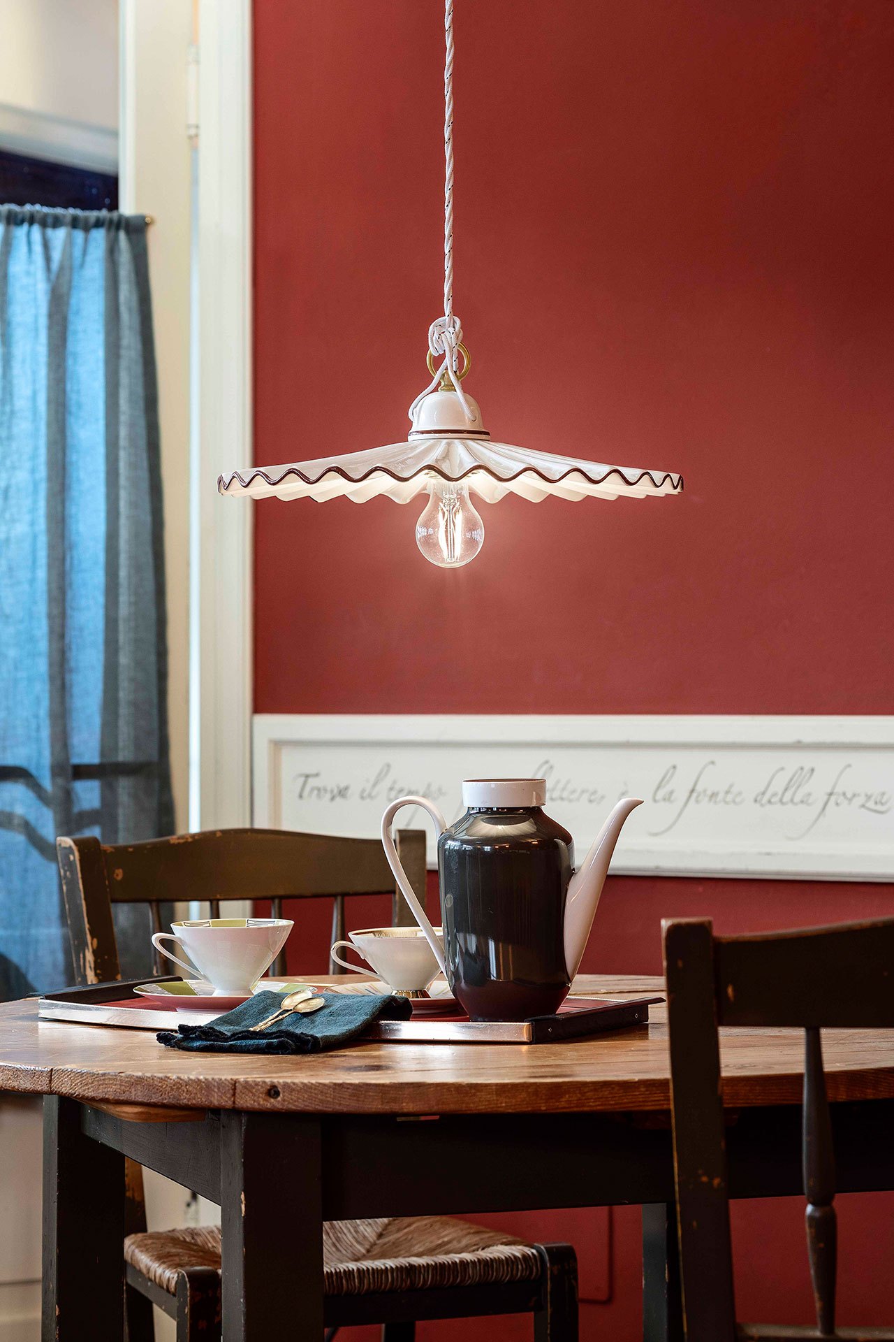 Angolo pranzo con la parete rossa e la sospensione Ferroluce in ceramica bianca sopra il tavolo: la stessa scena al buio e con la luce accesa