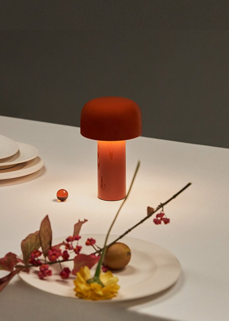 Lampada portatile Flos Bellhop rossa su un tavolo con frutta e fiori