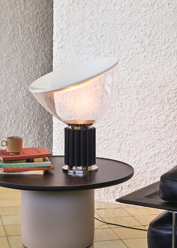 Lampada da tavolo Flos Taccia con il diffusore di vetro su un tavolino, accanto a una tazza