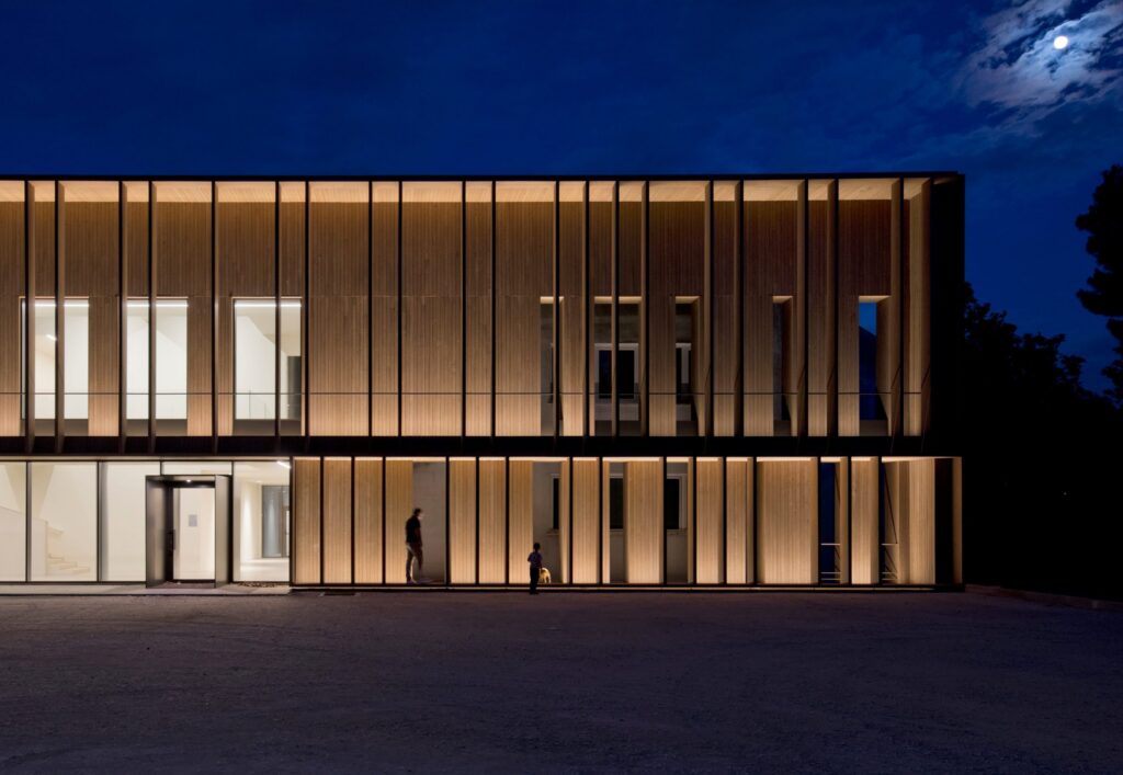 Facciata in legno e vetro illuminata di sera con le linee iGuzzini Linealuce