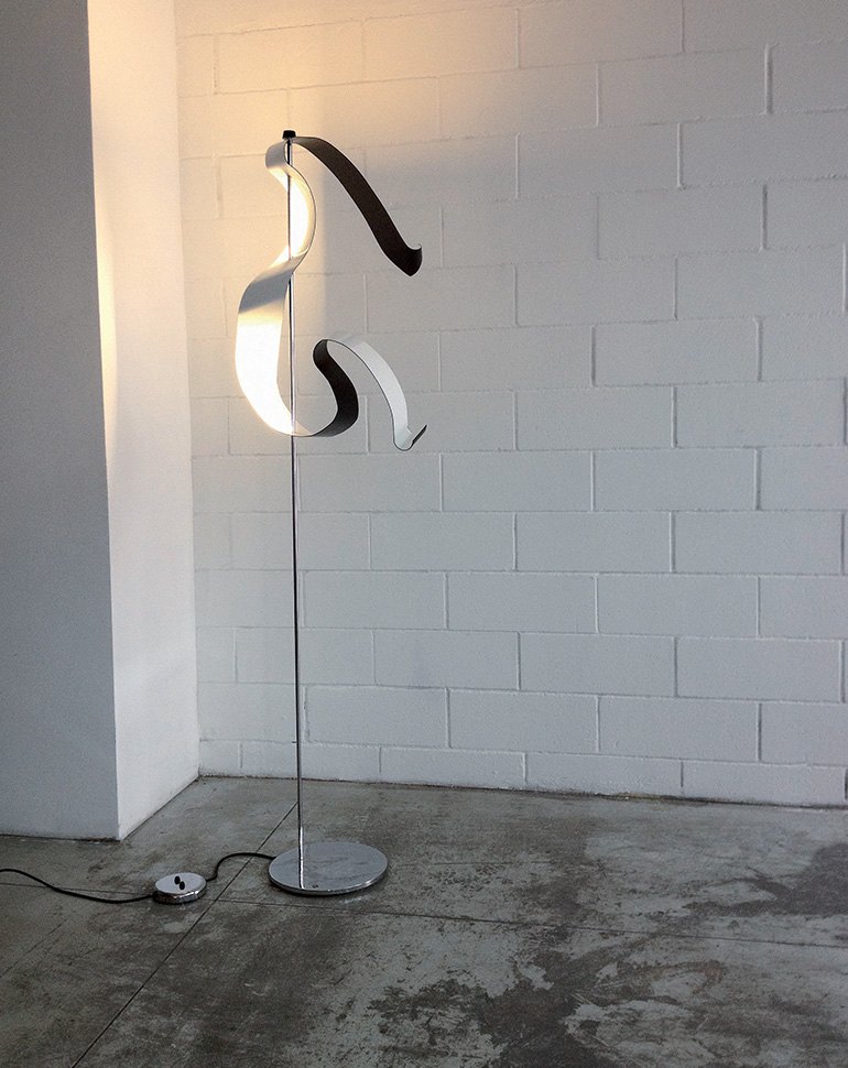 Lampada da terra Knikerboker Curve con la lama di metallo curva accanto a un muro bianco