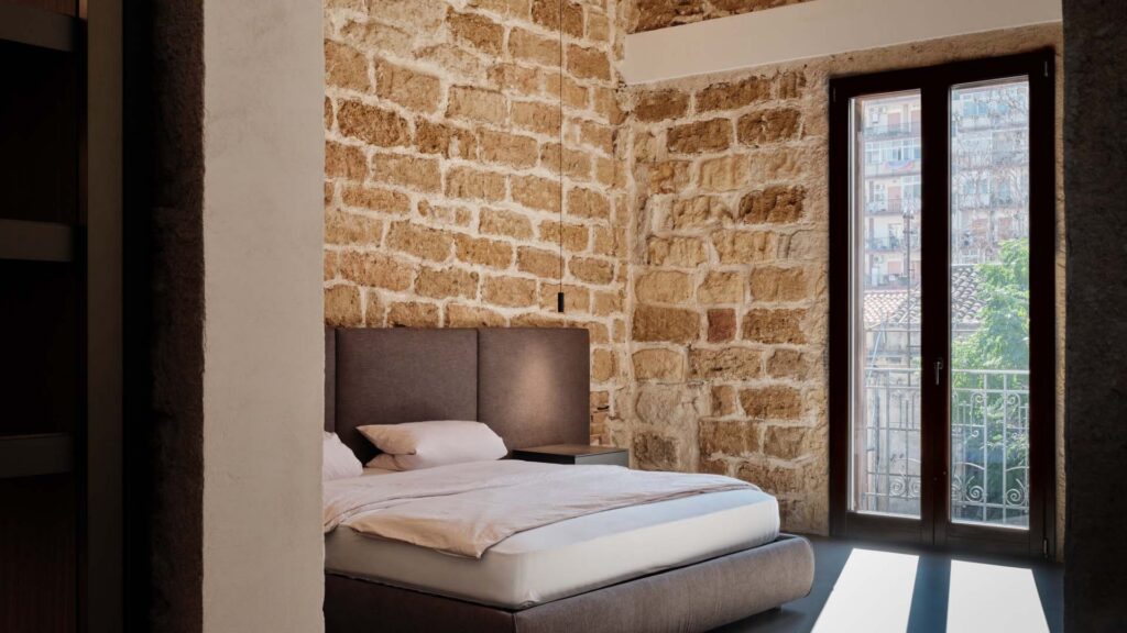 Camera da letto con la parete in pietra illuminata dagli apparecchi Linea Light