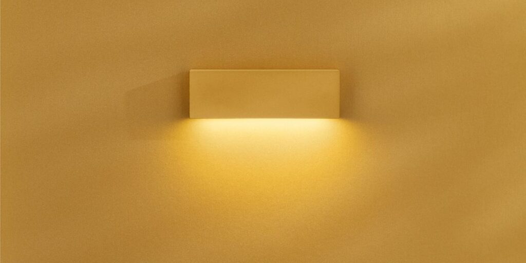 Applique Lombardo Tape con luce verso il basso, su parete gialla