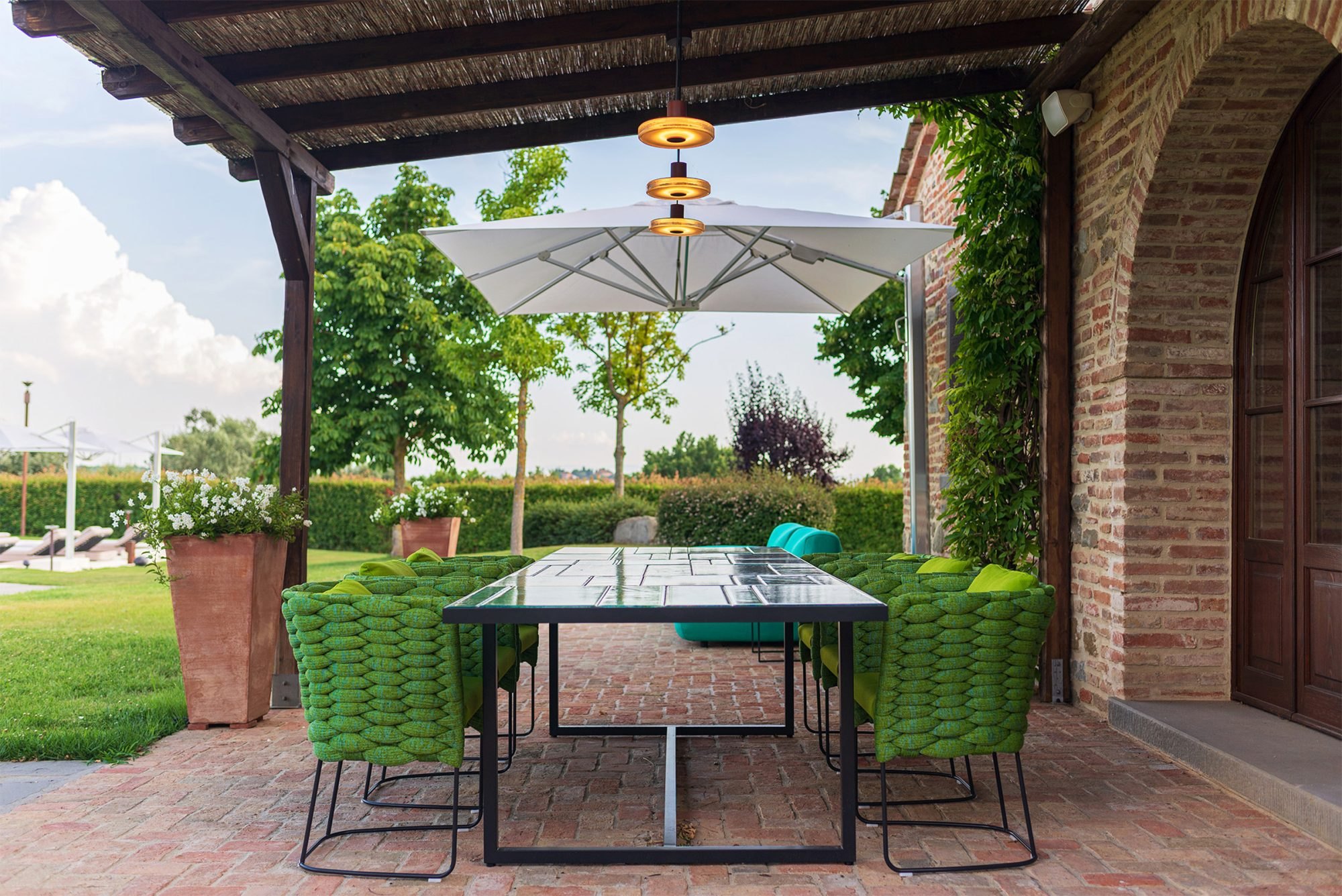 Pergola di una villa in Toscana con il tavolo apparecchiato e le lampade Panzeri accese: la stessa scena al buio e con la luce accesa