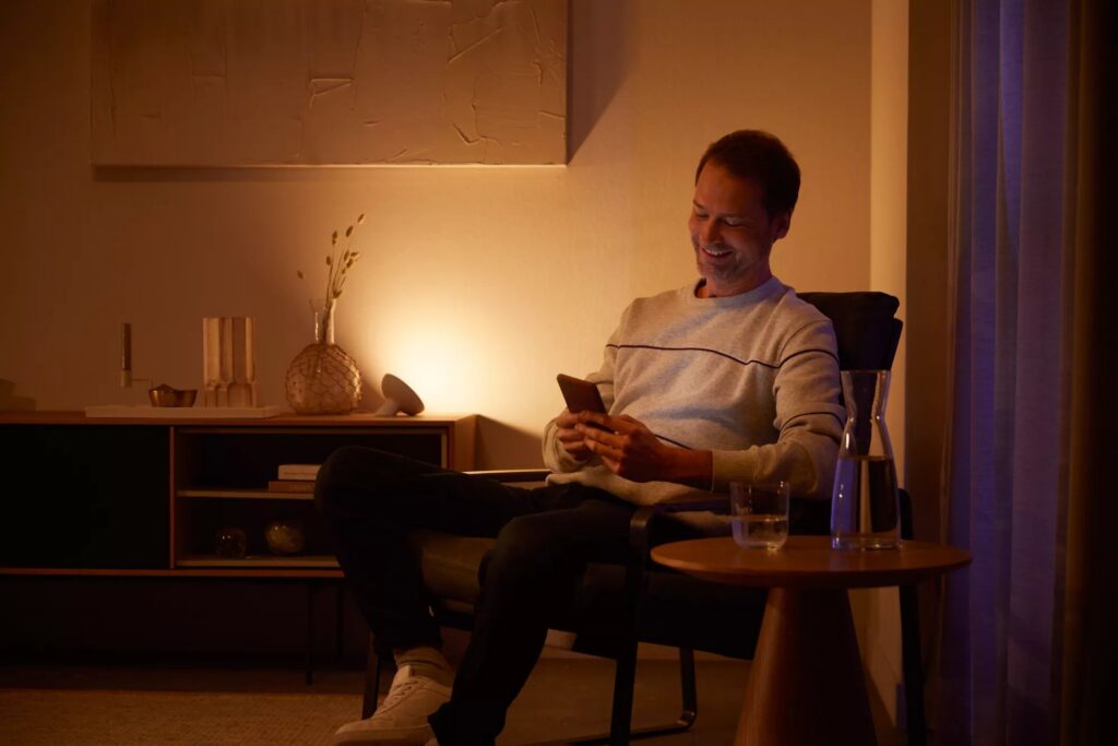 Persona che legge in poltrona accanto alla lampada Philips Hue Bloom accesa