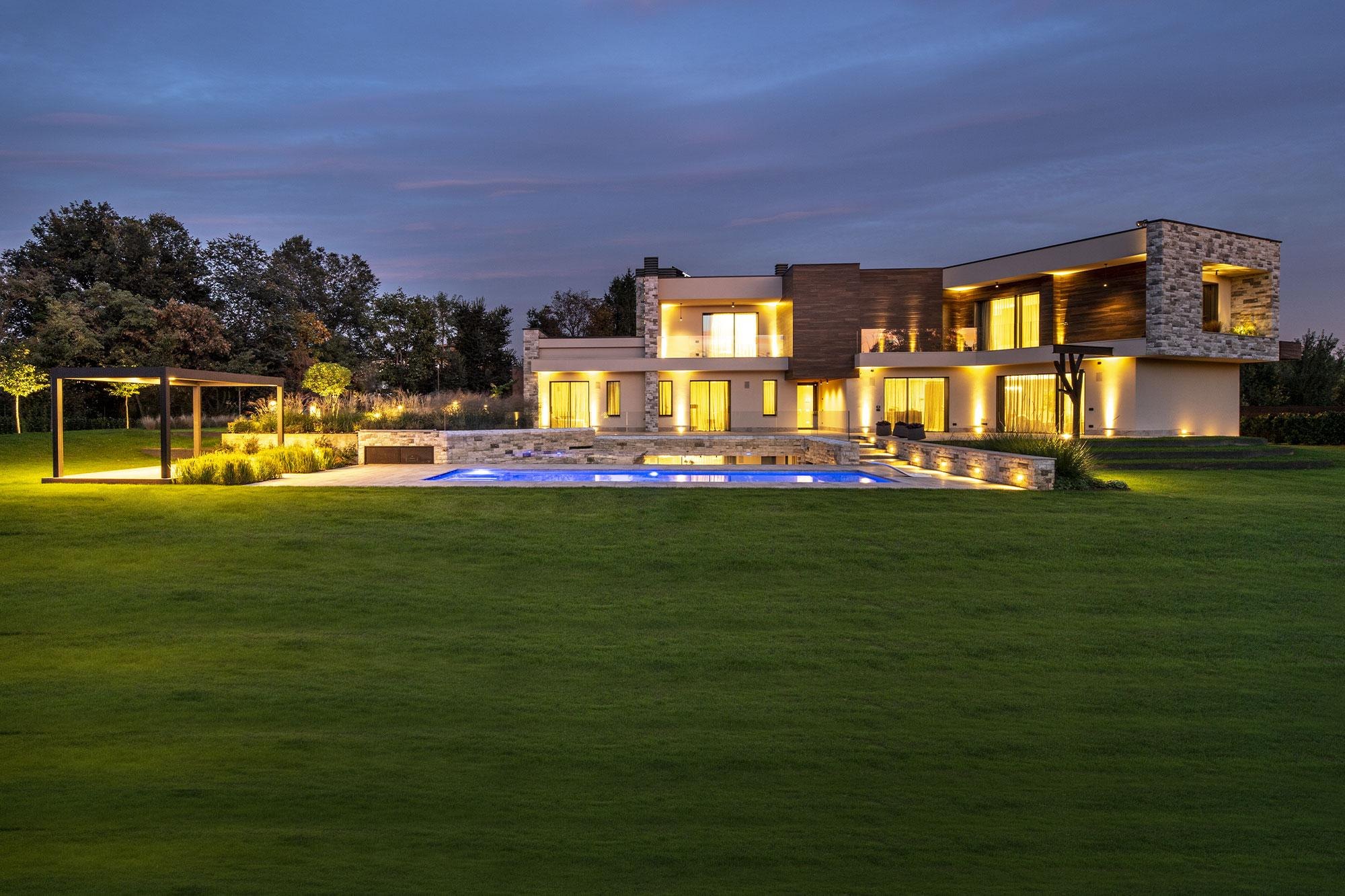 Villa in pietra con il prato e il vialetto illuminati dai paletti e dagli incassi Platek: la stessa scena al buio e con la luce accesa