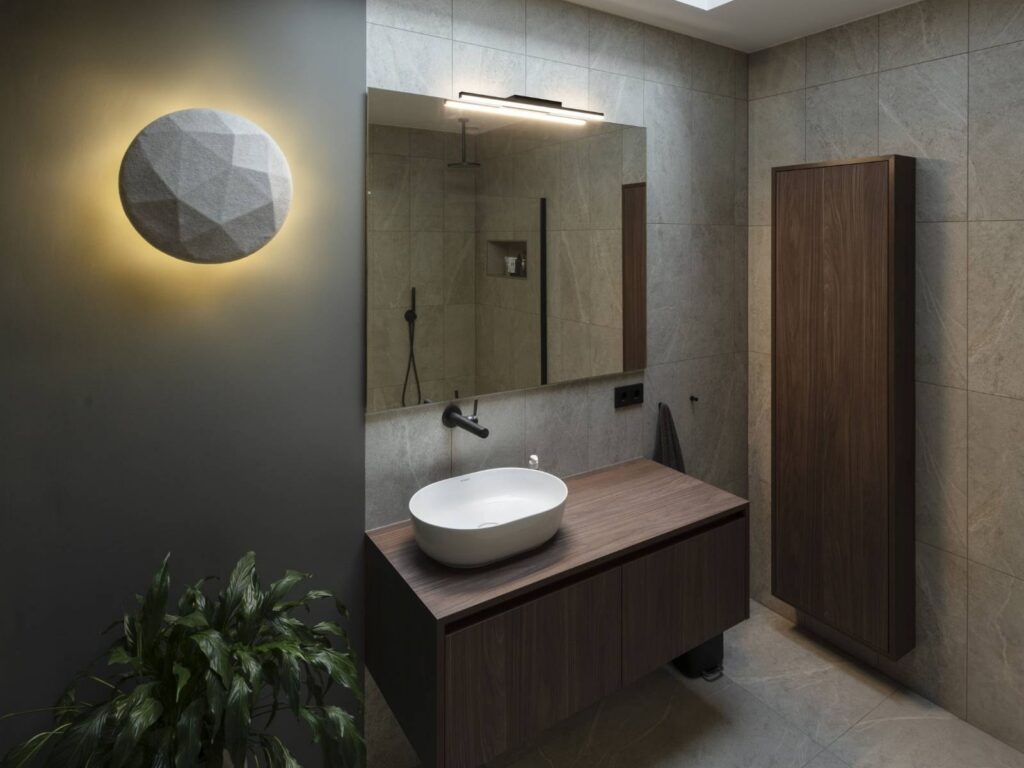 Bagno con il mobile in legno, lo specchio e l'applique tonda SLV accesa a parete