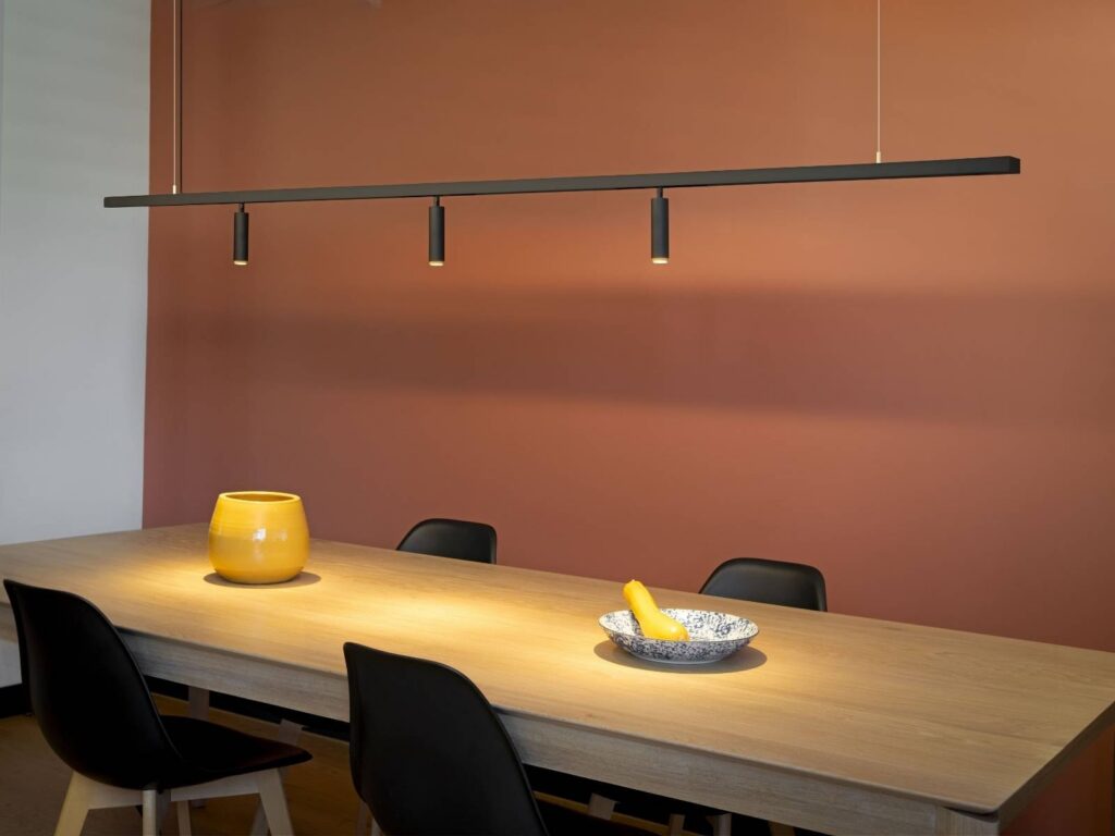 Sala da pranzo con la parete arancione e il binario SLV con i faretti sopra il tavolo