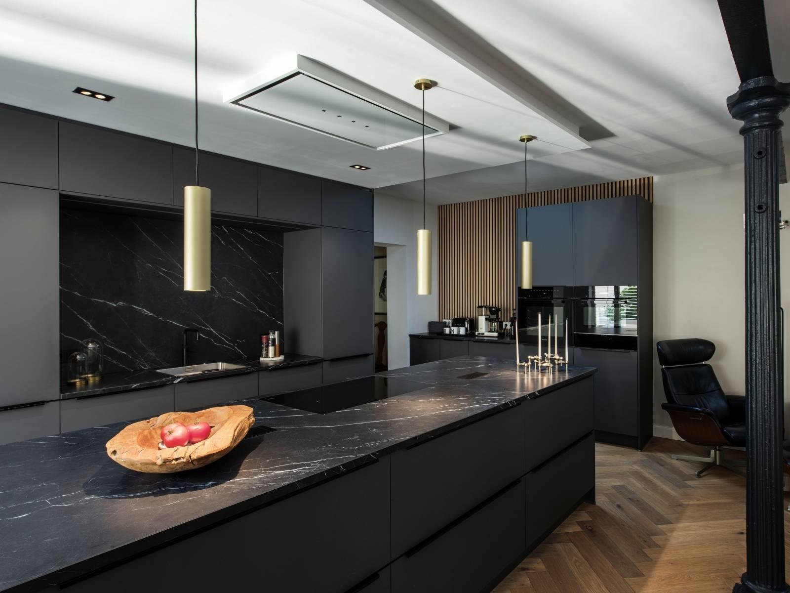 Cucina scura con l'isola in marmo nero e le sospensioni SLV accese sopra: la stessa scena al buio e con la luce accesa