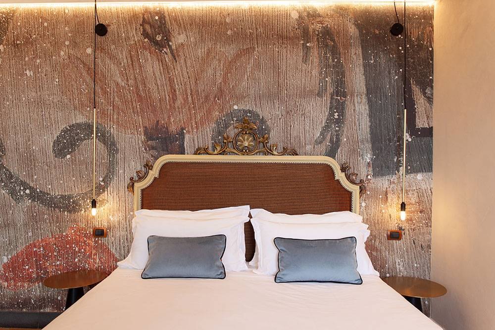 Camera d'albergo con la parete affrescata illuminata dalle applique Vesoi: la stessa scena al buio e con la luce accesa