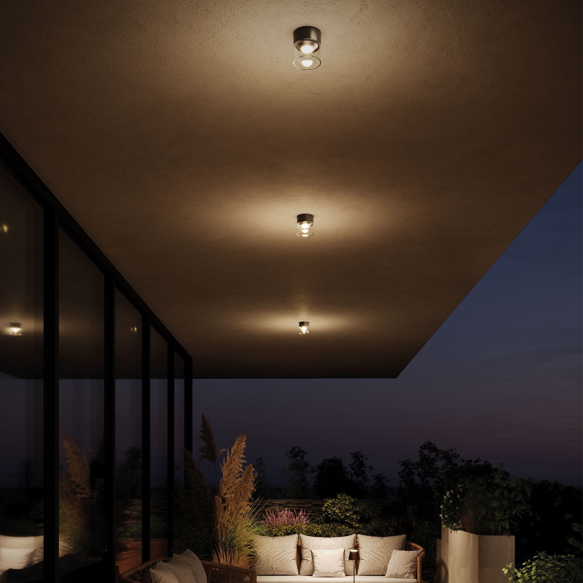 Terrazza di sera con le lampade da esterno Zafferano a soffitto e il divano: la stessa scena al buio e con la luce accesa