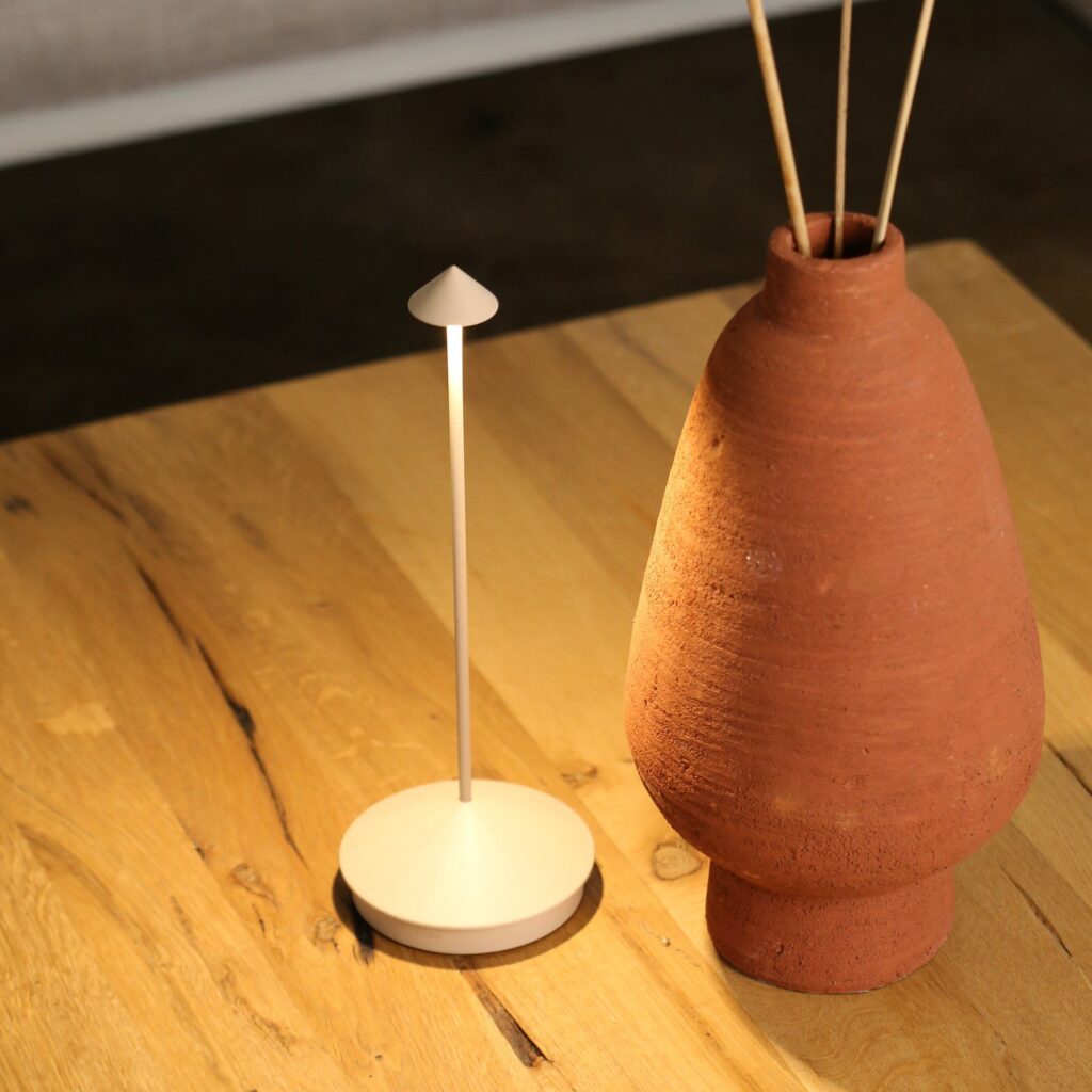 Lampada portatile Zafferano Pina bianca su un tavolo di legno accanto a un vaso